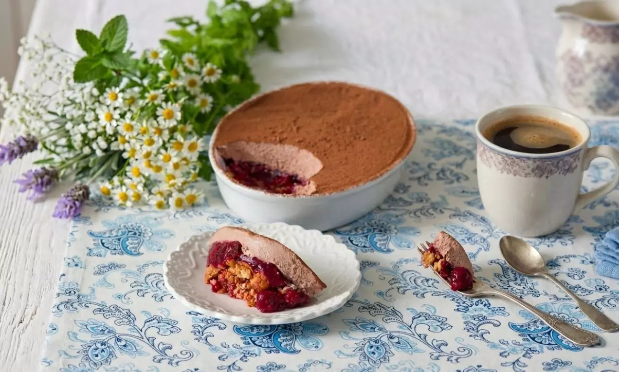 Jemná vrstva kakaa na hladkém krémovém povrchu tvarohového tiramisu s malinovým přelivem, podávané na vzorovaném talíři vedle kávy