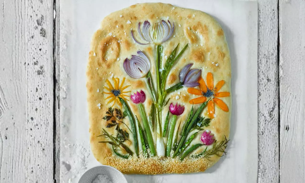 Zlatavá focaccia s květinovým vzorem z barevné zeleniny, struktura jemně porézní, zdobená hrubou solí na jednoduchém podkladu