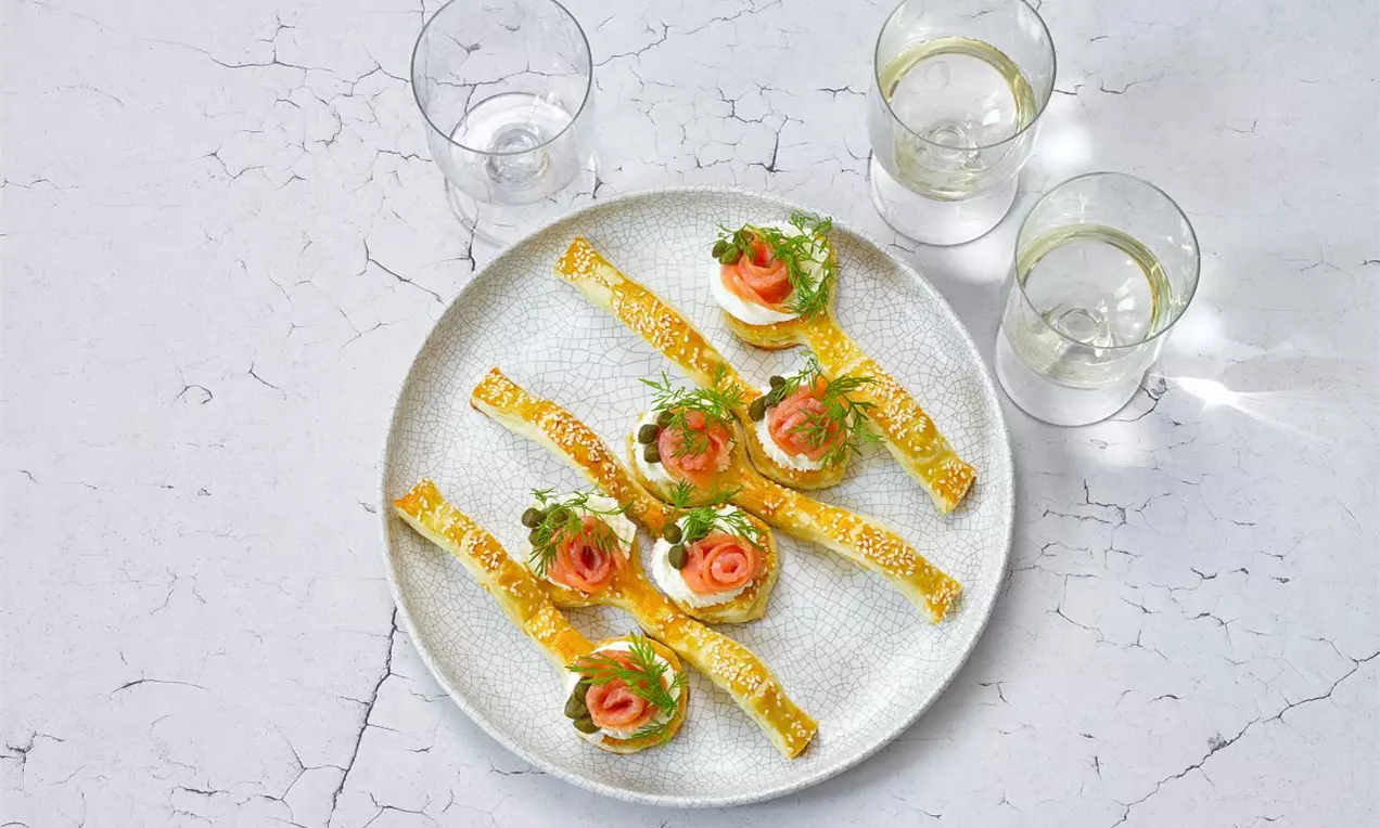 Kanapky s lososem na kulatém talíři, zlatavé křupavé pásky, svěží růžový losos, zdobené zelenými lístky petržele a sklenice sektu