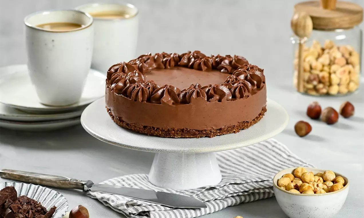Kulatý veganský čokoládový dort s hladkým lesklým povrchem a bohatou dekorací čokoládových krémových spirál na světlém stojanu