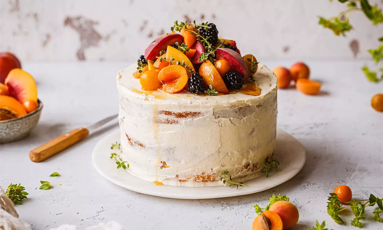 bílý vanilkový dort na bílém stole a bílém talířku ozdobený ovocem a politý sirupem.