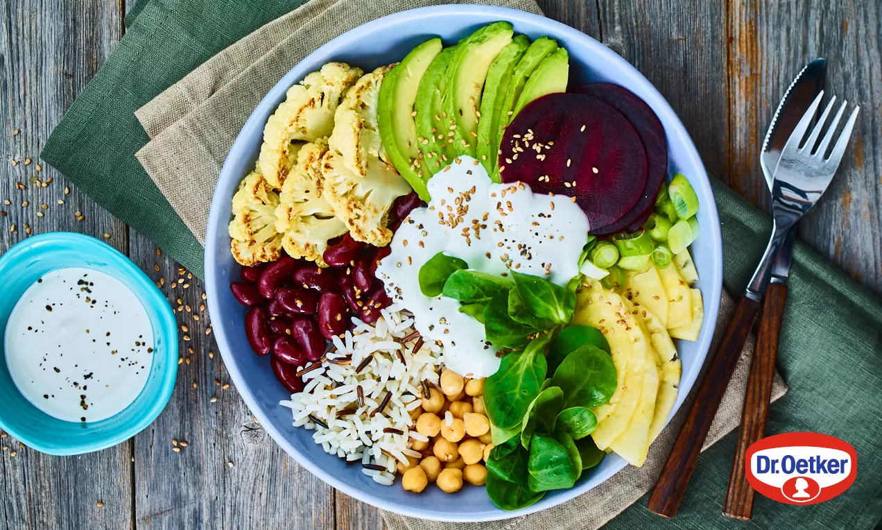 Veganská Buddhova miska s avokádem, červenou řepou, rýží, cizrnou, fazolemi, špenátem, mangem, květákem a bílým dipem na šedém talíři