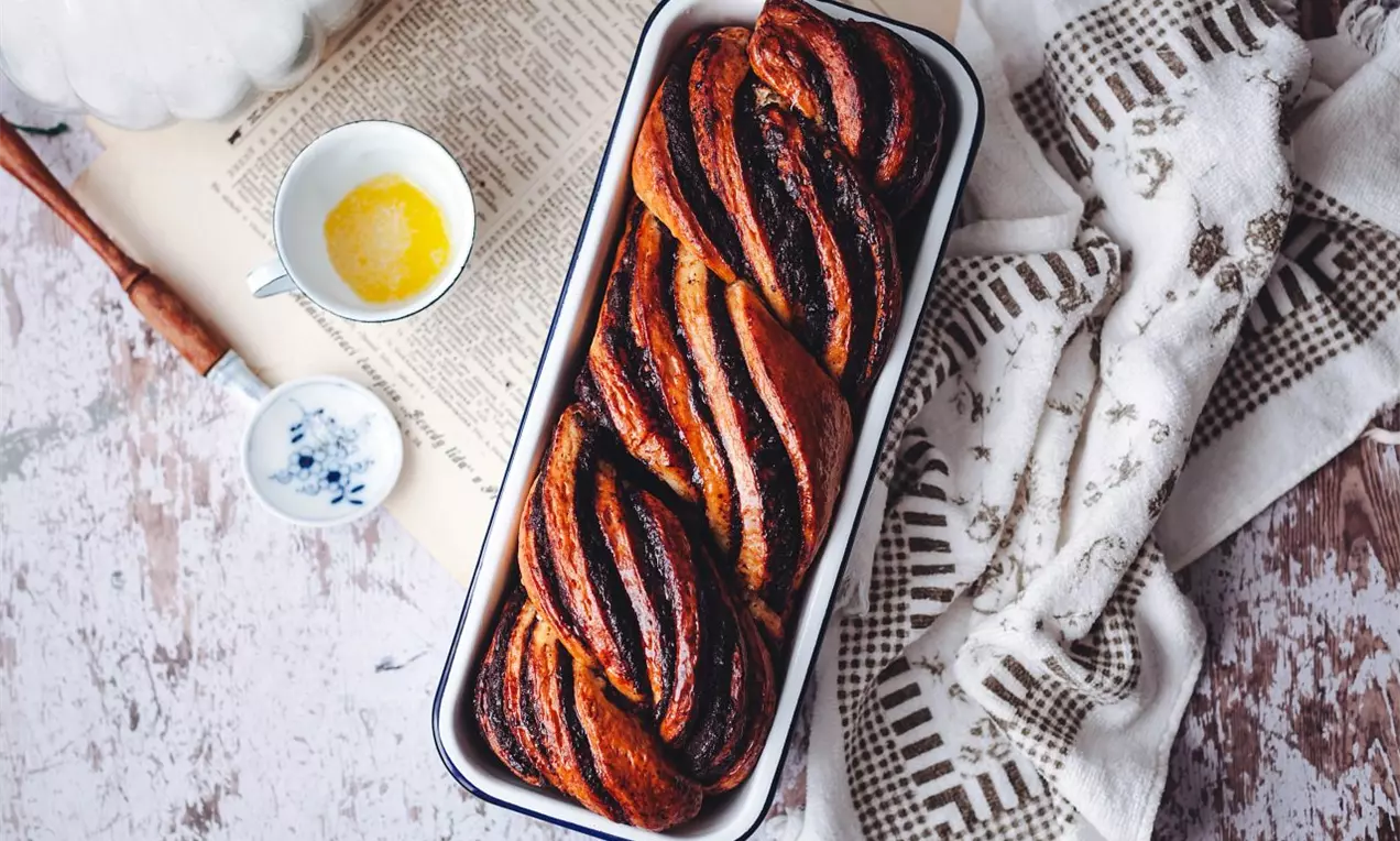 Zamotaný dvoubarevný moučník ve formě na biskupský chlebíček na dřevěné bílé desce se lněnou utěrkou po pravé straně