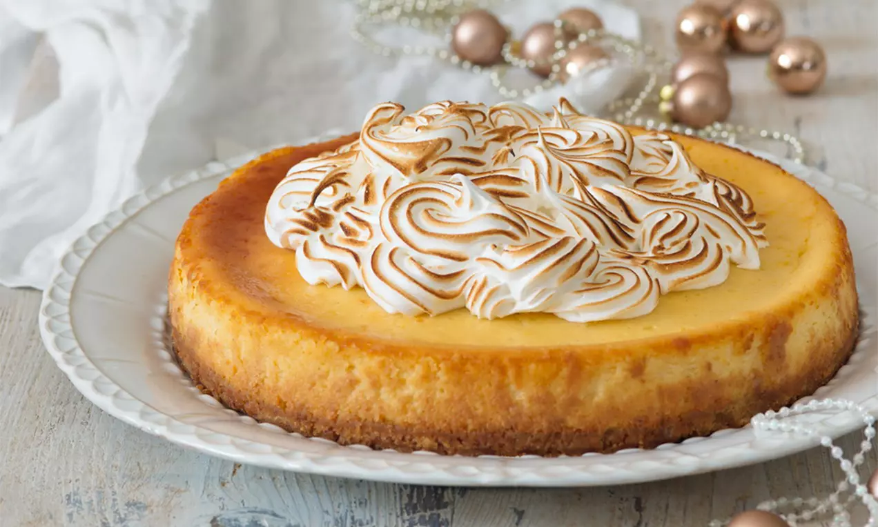 Citrónový cheesecake se zlatavou kůrkou, jemným žlutým středem a nadýchanými bílými pusinkami s karamelizovanými šmouhami na bílém talíři