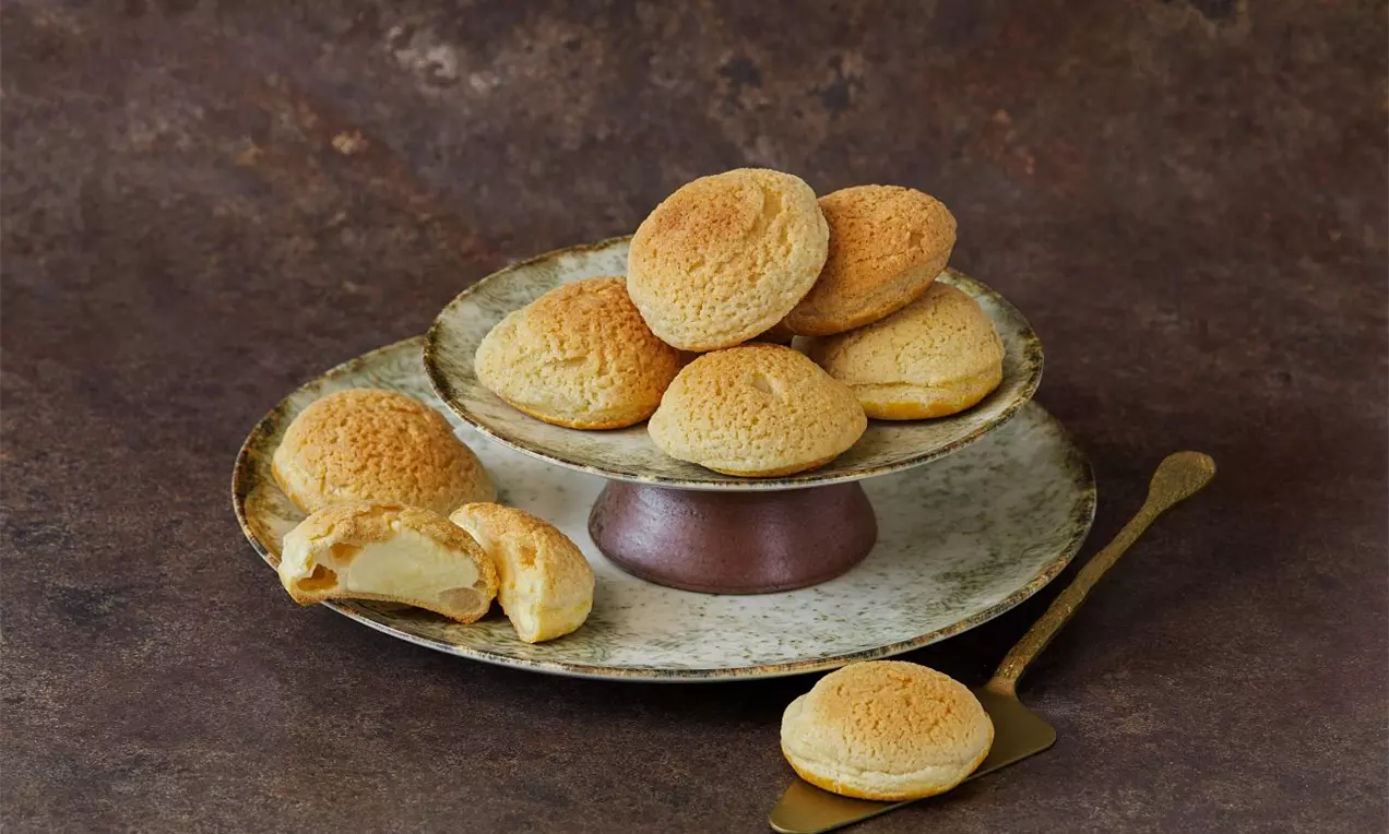 Odpalované kuličky se zlatavou křupavou krustou na rustikálním keramickém talíři, jedna rozkrojená s jemným vanilkovým krémem uvnitř