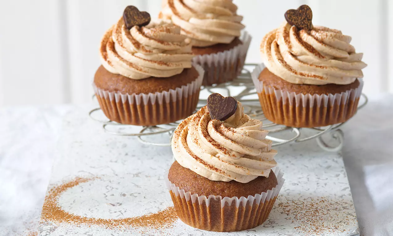 Perníkové cupcakes s hnědým základem, krémovou šlehačkou posypanou skořicí, zdobené čokoládovým srdcem na mřížce a jemném podkladu
