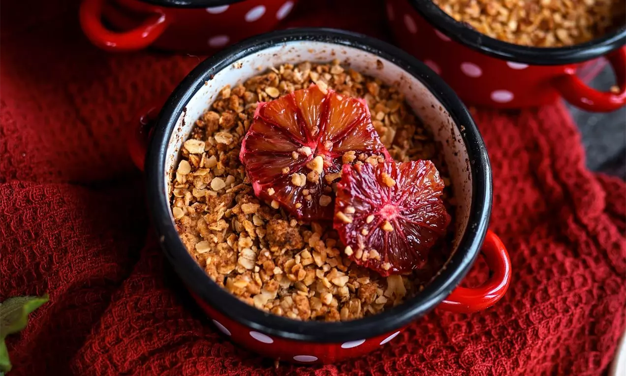 Miska se zapečeným crmble zdobená červeným pomerančem na červeném podkladu