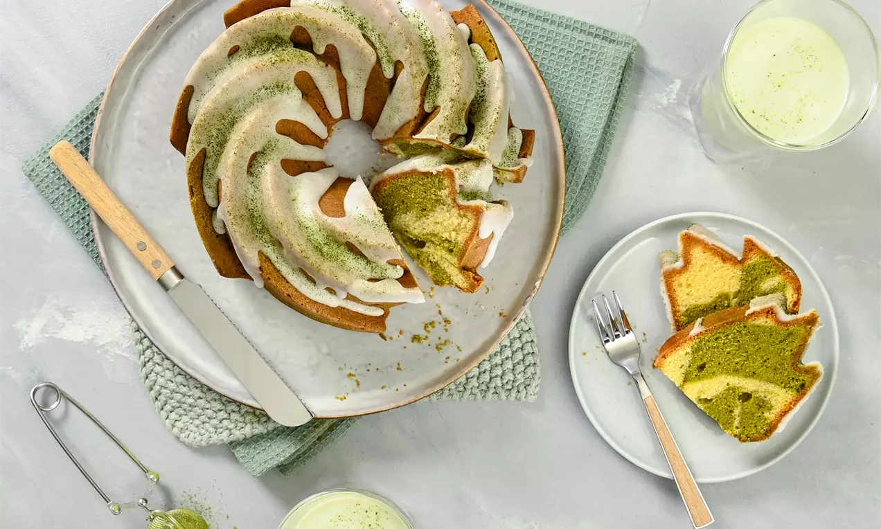 Vegan bábovka ve tvaru kruhové spirály, dvoubarevné vrstvy zelené a světlé hnědé, zdobená bílou polevou a zeleným práškem na keramickém talíři