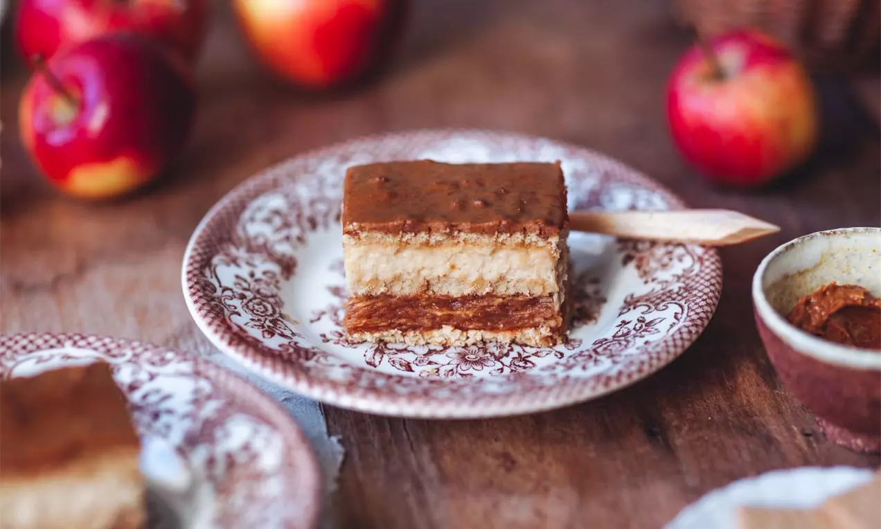 vrstvený dezert se světlým korpusem světlou a hnědou karamelovou vrstvou a karamelovou polevou servírovaný na zdobeném dezertním talířku na dřevěné desce