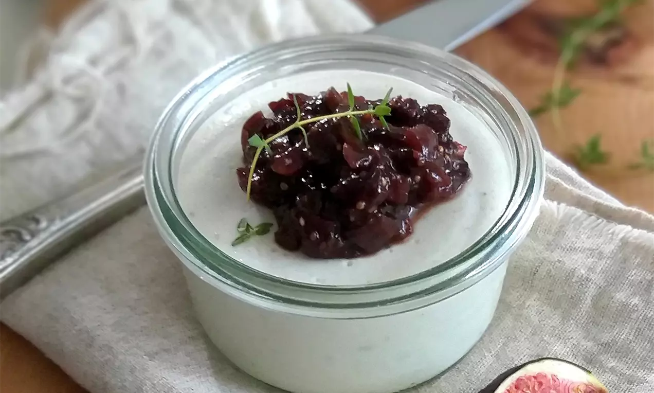 Jemný krém světle modré barvy v průhledném skleněném misce, ozdobený tmavě červeným ovocným chutney a lístkem čerstvého tymiánu