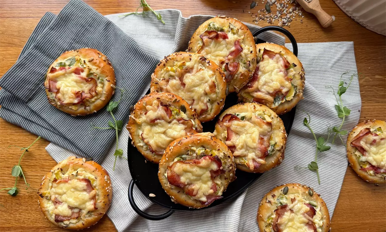 Kynuté koláče se slaninou a sýrem posypané semínky naaranžované na černém servírovacím podnosu a lněných utěrkách na dřevěném stole