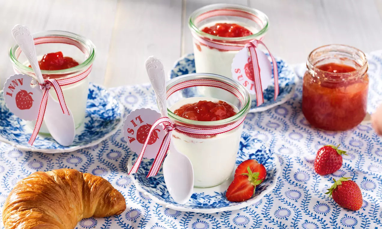Skleničky s bílým jogurtem ozdobeným jahodovo-grapefruitovým džemem, na modrých talířcích s krajkovým vzorem vedle čerstvých jahod a croissantu