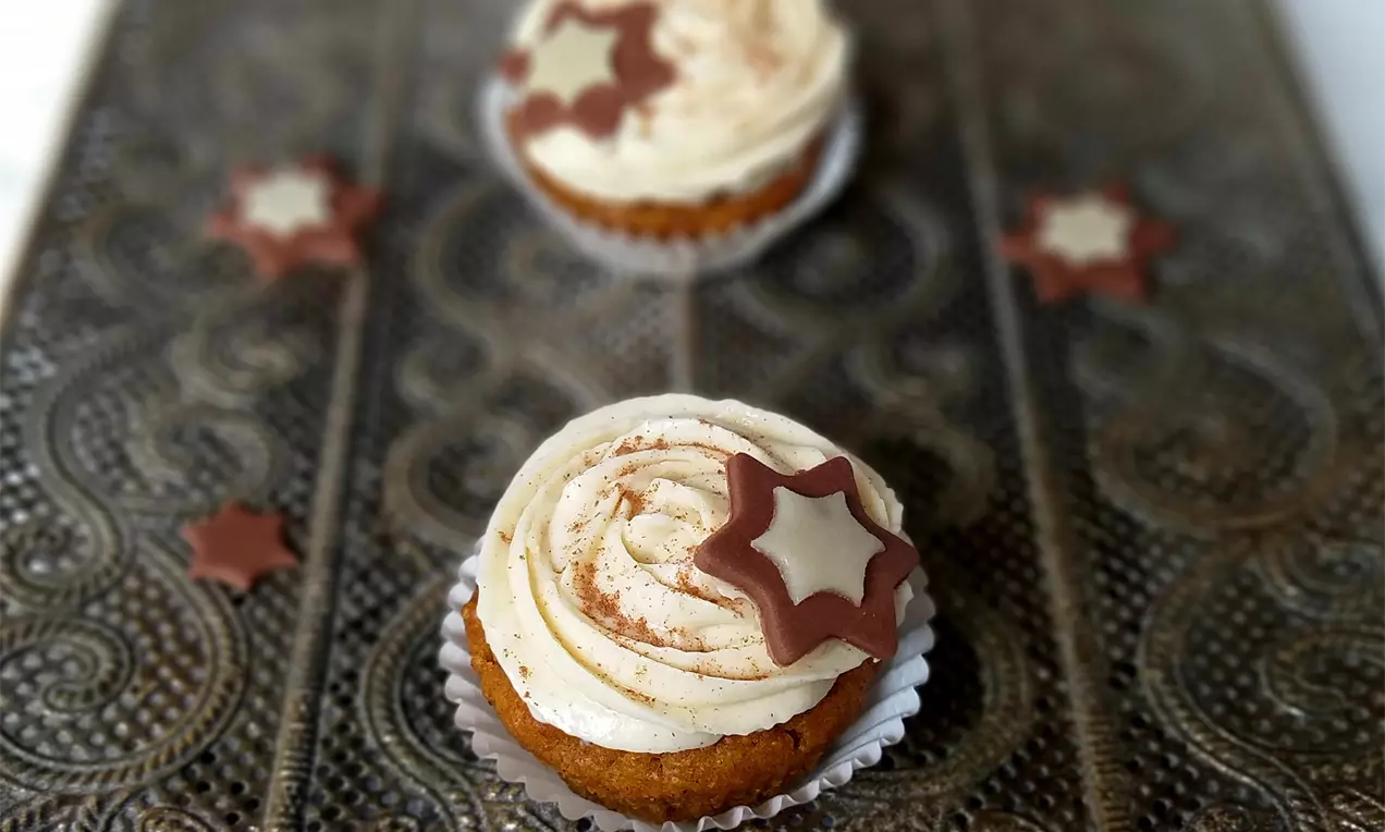 Perníkové cupcakes v bílých košíčcích s jemným kakaovým fondánem, zdobené krémovou spirálou a hvězdami z čokolády na ornamentálním podnosu