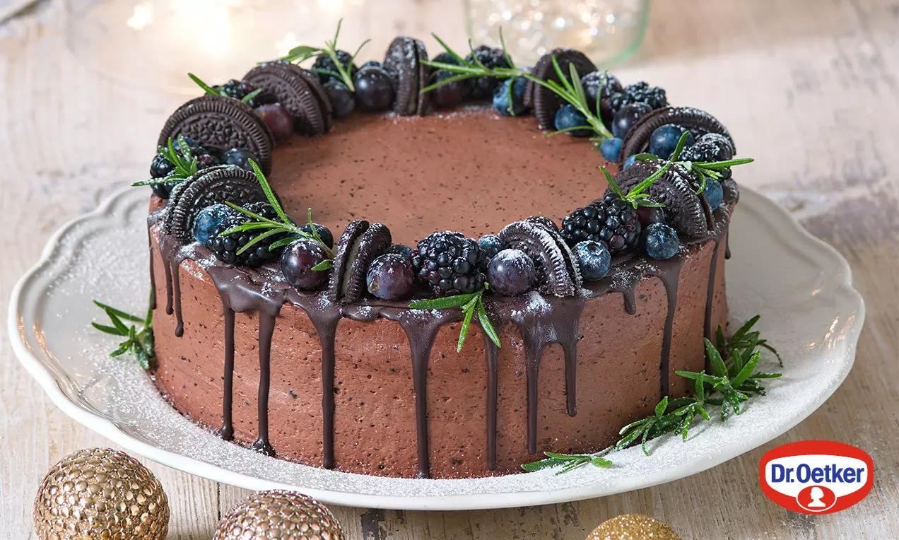 Dvoubarevný čokoládový dort s lesklou ganache, zdobený ostružinami, borůvkami, sušenkami a snítkami zelené na světle zdobeném talíři